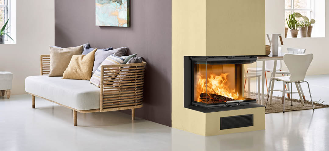 A fireplace painted yellow in a white room with a kitchen on one side and a sofa on the other