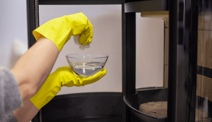 Hands with yellow rubber gloves holding a deep bowl with liquid and paper
