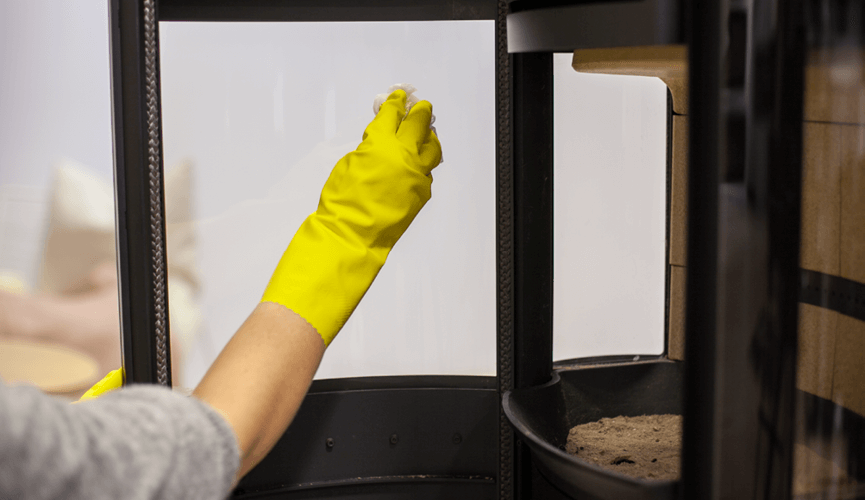 Hand with yellow rubber gloves cleaning the fireplace glass