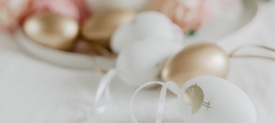 Table with white table cloth and decorative Easter eggs in gold, pink and white 