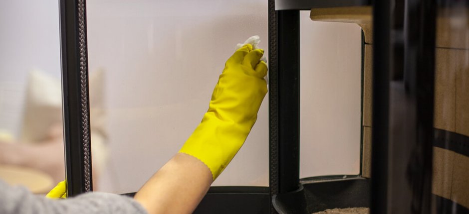 Hand with yellow rubber glove that washes soot off the fireplace glass on an oven