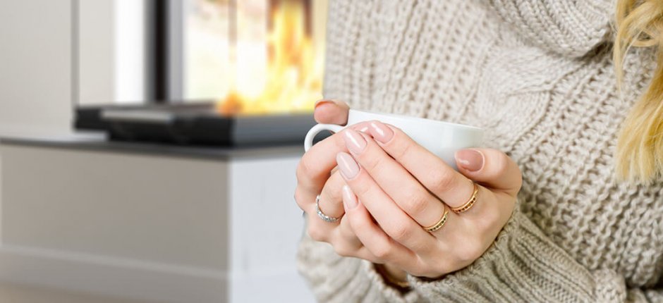 Hands holding a white cup of hot beverage in front of a fireplace