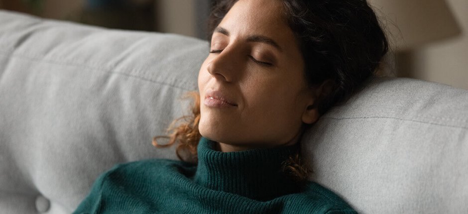 Woman with dark curly hair rests in a white chair by a black fireplace 