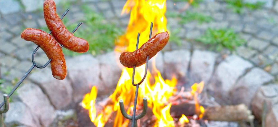 Grill sausages with sausage sticks over a fire outdoors in a fire pan