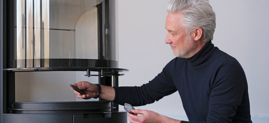 Middle-aged man in high-necked sweater designer Niels Kjeldsen shows glass handles in front of fireplace Scan 87
