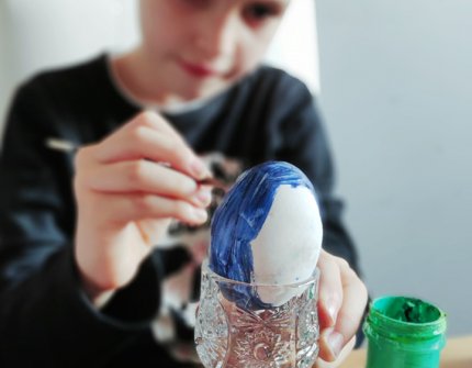 Boy sitting at a table and painting Easter eggs blue