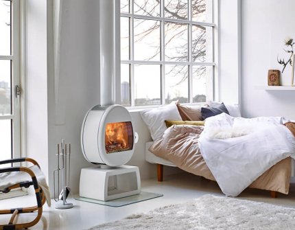 White fireplace Scan 66 with square stands in a white bedroom with large windows by a bed
